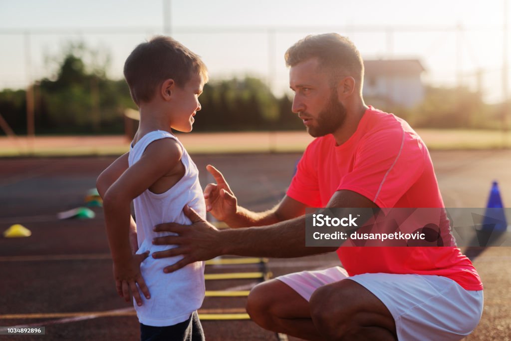 Sérieux jeune entraîneur donnant lecture d’un petit garçon à cause de son mauvais agir sur la formation. - Photo de Entraîneur libre de droits