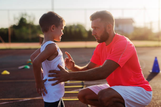 serious young trainer giving lecture to a little boy because of his bad acting on training. - tennis teenager little boys playing imagens e fotografias de stock