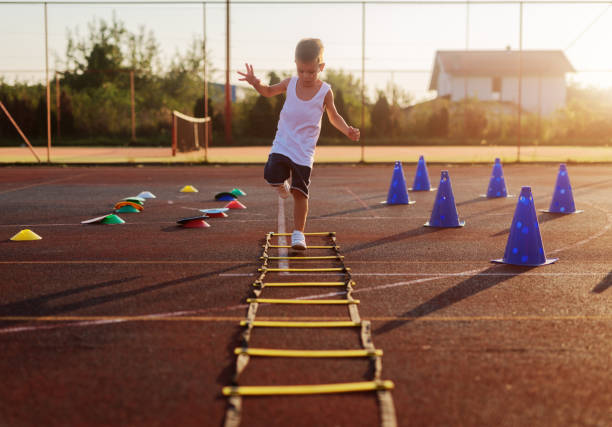 petit garçon sur l’entraînement d’été tôt le matin sautant par-dessus les entraves dans le domaine de la formation. - school sports photos et images de collection