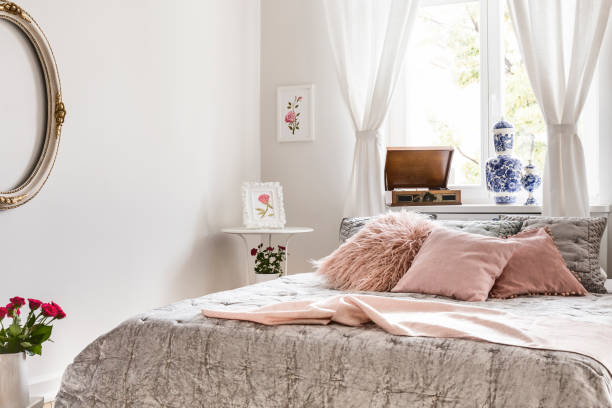 istock Soft gray and lemonade pink bedding and pillows on a bed which is standing against a bright window in an English style bedroom interior. Real photo. 1034893446