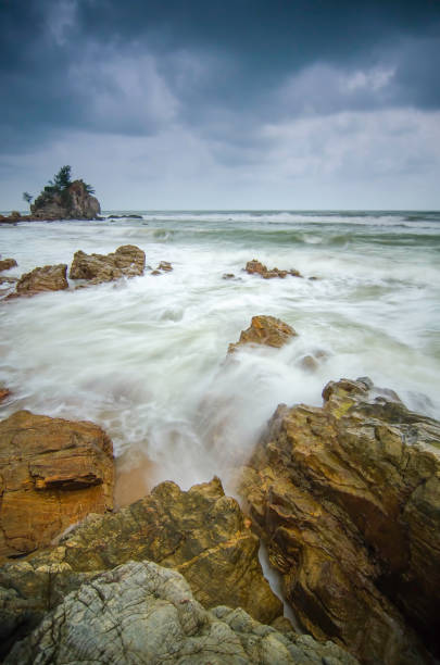 bella spiaggia con roccia che colpisce dalle onde. messa a fuoco morbida a causa della lunga esposizione. drammatiche nuvole scure e isola rocciosa - beauty in nature cloud rocky coastline rock foto e immagini stock