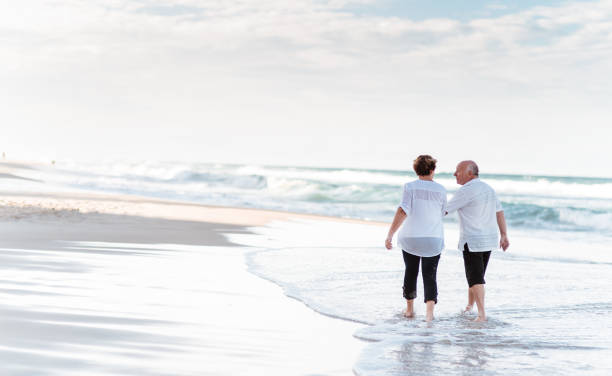 casal sênior de felicidade andando juntos na praia - senior couple senior adult pension couple - fotografias e filmes do acervo