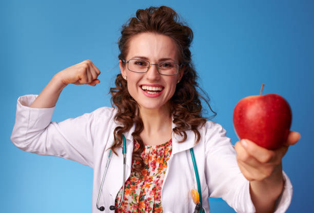 donna paediatrista dando una mela e mostrando bicipiti su blu - 13431 foto e immagini stock