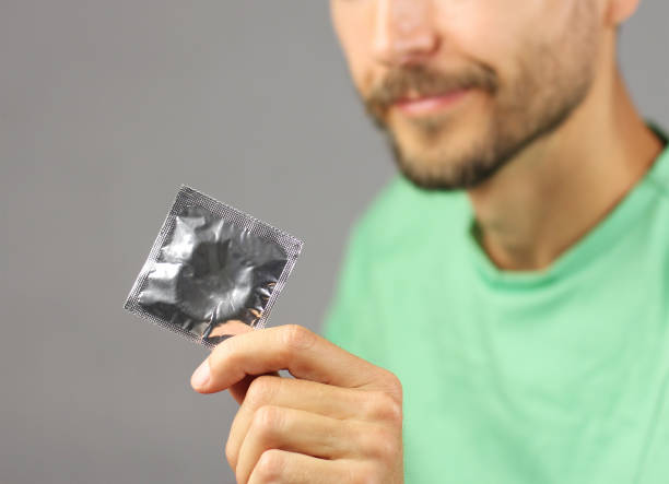 человек в зеленой рубашке держит презерватив в руке и улыбается, концепция контроля над рождаемостью - care condom confidence contraceptive стоковые фото и изображения