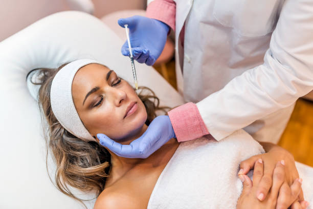 Getting some help with those wrinkles... Photo of doctor cosmetologist makes Lip augmentation procedure of a beautiful woman in a beauty salon.Cosmetology skin care. Close up of hands of cosmetologist making Botox injection in female lips. He is holding syringe. Mature  beautiful Caucasian woman is receiving procedure with enjoyment. beauty clinic stock pictures, royalty-free photos & images