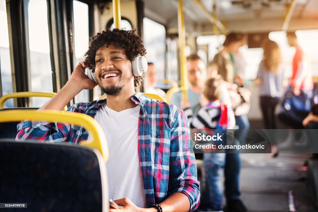 Young Afro-American man is sitting in a bus with headset on his head and listening to the music. Bus Stock Photo