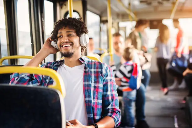 Photo of Young Afro-American man is sitting in a bus with headset on his head and listening to the music.