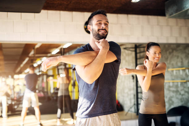 fuerte joven sonriendo a los atletas que se extiende en un gimnasio. - hombro fotografías e imágenes de stock