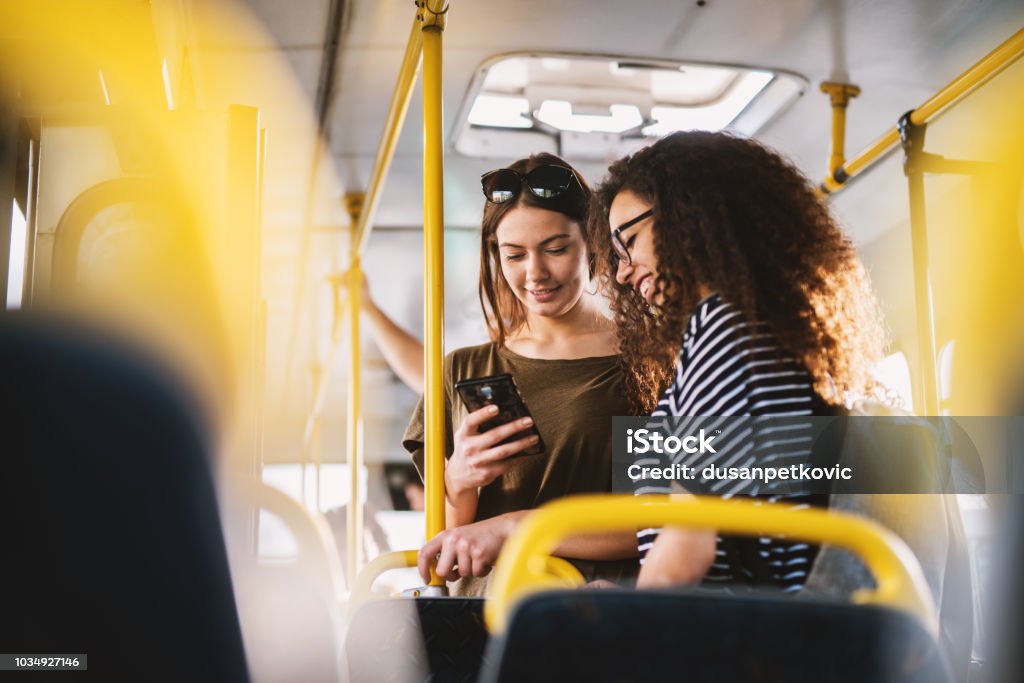 Two best young sweet girl friends standing in a bus and looking in a telephone. Bus Stock Photo
