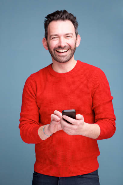 istock cheerful man with beard holding mobile phone against blue background 1034931512