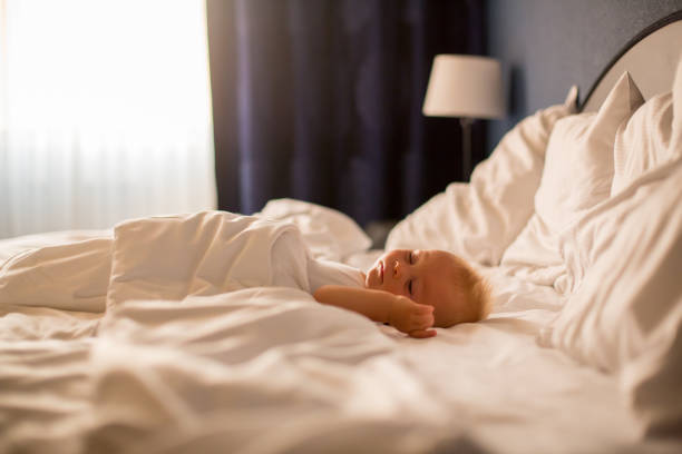 Photo of newborn baby girl sleeping on bed. Her eyes are closed.  Selective focus on models little fingers. Shot indoor with a full frame mirrorless camera. Daylight is used.