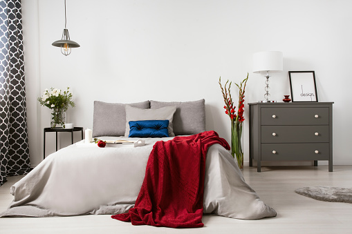 Real photo of a romantic bedroom interior with a big bed, red blanket, rose and commode