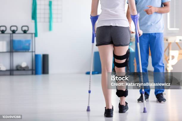 Patient With Stiffener On The Leg Walking With Crutches During Rehabilitation Stock Photo - Download Image Now