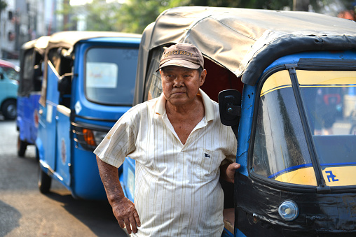 Local tuc tuc driver by his vehicle on a sunny day in Jakarta, Indonesia