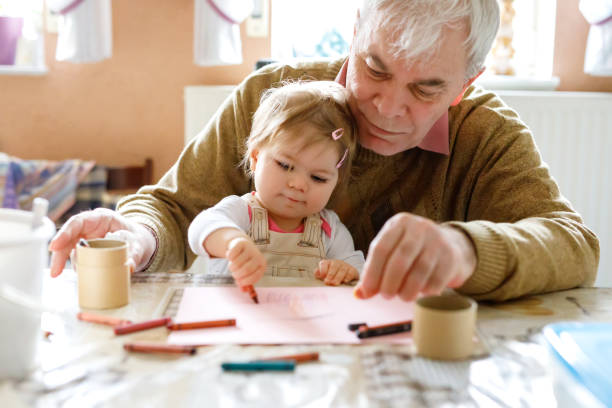 Cute little baby toddler girl and handsome senior grandfather painting with colorful pencils at home. Grandchild and man having fun together Cute little baby toddler girl and handsome senior grandfather painting with colorful pencils at home. Grandchild and man having fun together. Family and generation in love. old man baby stock pictures, royalty-free photos & images