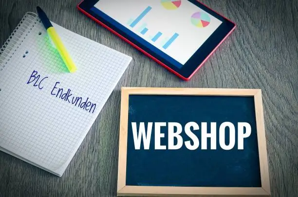 Plate with the inscription Webshop and the german Words B2C Endkunden in english B2C end customers (Business to consumer) with a tablet Graphs and statistics and block to illustrate the increase in sales of an online shop