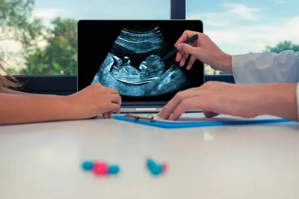 Doctor showing a scan of fetus on a laptop to a woman patient.