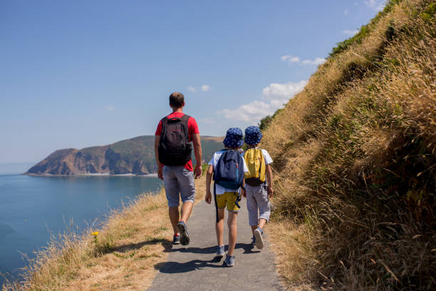 Father and two boys, family walking on a small path along the stunning Devonshire coastline near Lynmouth in Devon Father and two boys, family walking on a small path along the stunning Devonshire coastline near Lynmouth in Devon, England, UK devon stock pictures, royalty-free photos & images