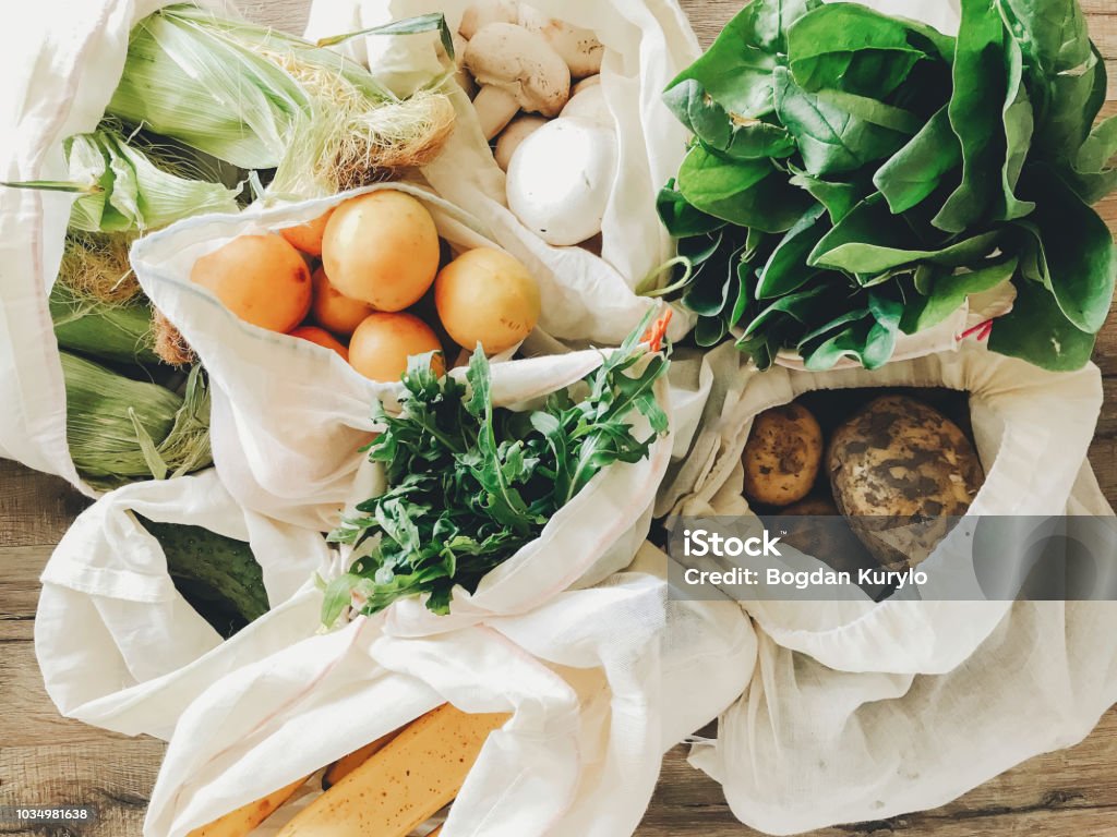 frisches Gemüse in Öko Baumwolltaschen am Tisch in der Küche. Kopfsalat, Mais, Kartoffeln, Aprikosen, Bananen, Rucola, Pilze vom Markt. Zero waste-shopping-Konzept.   Ban Kunststoff - Lizenzfrei Speisen Stock-Foto