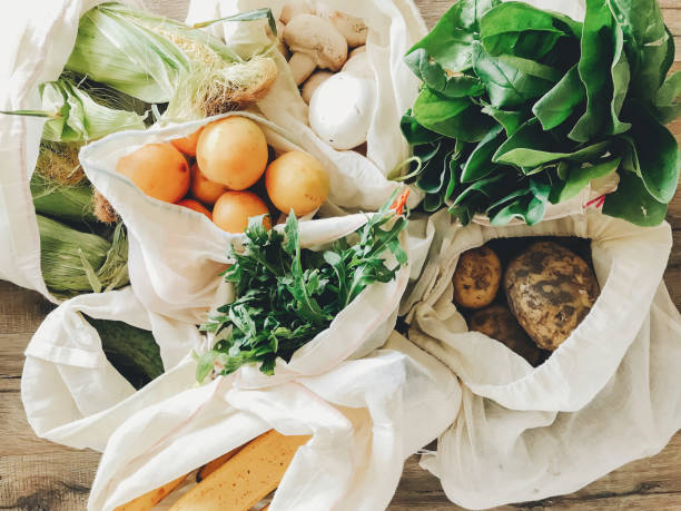 fresh vegetables in eco cotton bags on table in the kitchen. lettuce, corn, potatoes, apricots, bananas, rucola, mushrooms from market. zero waste shopping concept.   ban plastic - vegetable market imagens e fotografias de stock