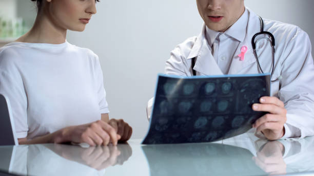 male doctor explaining young lady results of mammogram, breast cancer awareness - x ray image radiologist examining using voice imagens e fotografias de stock