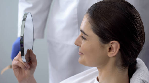 donna che si guarda allo specchio dopo la procedura cosmetica, soddisfazione per il risultato - nose job foto e immagini stock