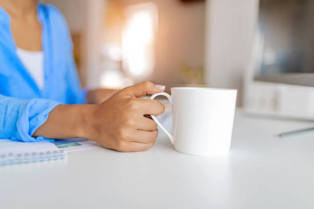 Nice Coffee! Woman Holding Coffee Cup While Sitting at Her Working Place. Cropped Image of Young Woman With Cup of Coffee Against Home Interior Background. Woman Working on Freelance Remotely From Her Home