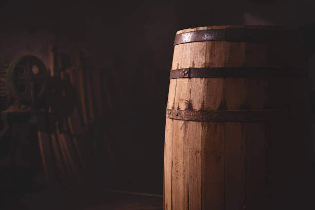 wooden barrel on a dark background, in a workshop, in an old room. wooden barrel on a dark background, in a workshop, in an old room. production of barrels for cognac and wine, in a low key legacy concept photos stock pictures, royalty-free photos & images