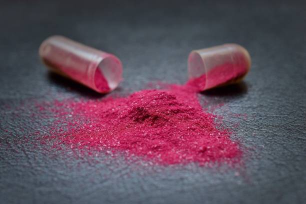 istock Shiny Pink Powder Spilled From Open Capsule On Table 1035005338