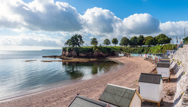 пляжные хижины и красные скалы у пляжа в торки, девон - torquay стоковые фото и изображения