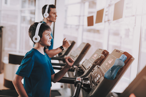 Young Father and Son Training on Treadmills in Gym. Healthy Lifestyle Concept. Sport and Training Concepts. Modern Sport Club. Sport Equipment. Family Sport. Running Tracks. Parent with Child.