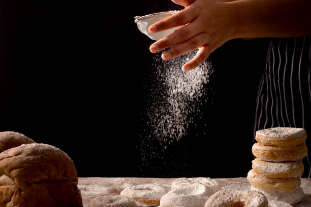 istock Chef hands sprinkling preparing bread dough and doughnuts with icing sugar on wooden table isolated on black background,Food concept. 1035016886