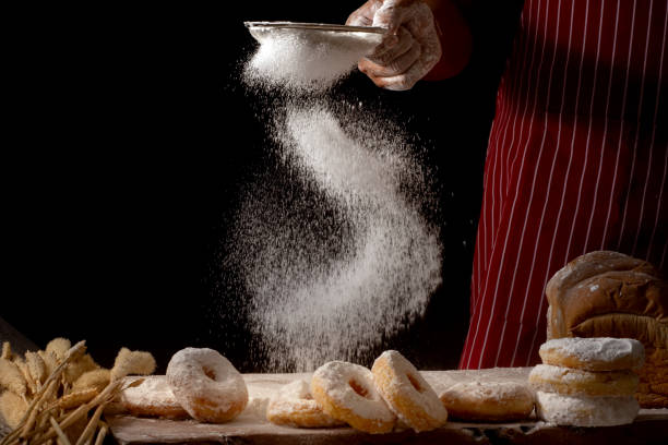 istock Chef hands sprinkling preparing bread dough and doughnuts with icing sugar on wooden table isolated on black background,Food concept. 1035016888