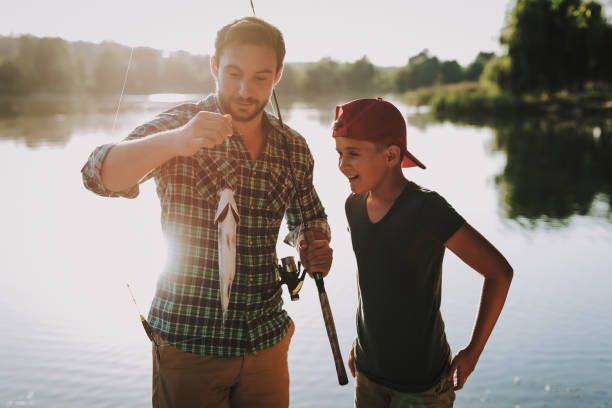 istock Young Father with Son in Cap Fishing on River. 1035027754