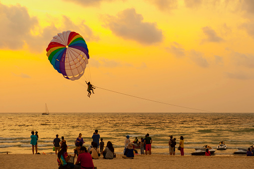 Patong Beach, Phuket, Thailand - March 4, 2015: Parasailing tourist takes off in the evening under a parachute towed behind a power boat from Patong beach, Phuket, Thailand.
