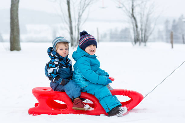 istock Two kid boys having fun sleigh ride during snowfall. Children sledding on snow. siblings riding a sledge. Twins play outdoors. Cute little toddlers sled on winter day. Active fun for family vacation 1035065192