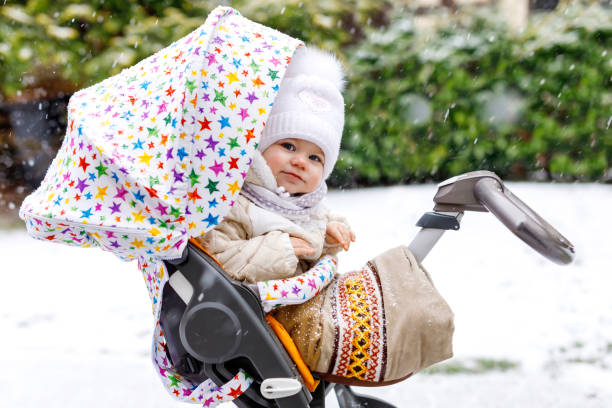 cute little beautiful baby girl sitting in the pram or stroller on cold day with sleet, rain and snow. happy smiling child in warm clothes, fashion stylish baby coat. baby with big umbrella. - smiling little girls little boys autumn imagens e fotografias de stock