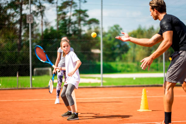 Young man teaching two girls playing tennis Young caucasian man teaching two little girls playing tennis. tennis coach stock pictures, royalty-free photos & images
