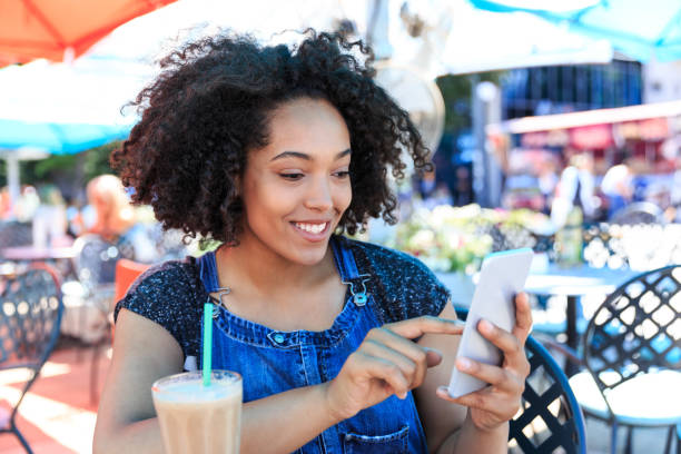 istock Smiling african woman drinking cocktail in cafeteria and using smart phone 1035073302