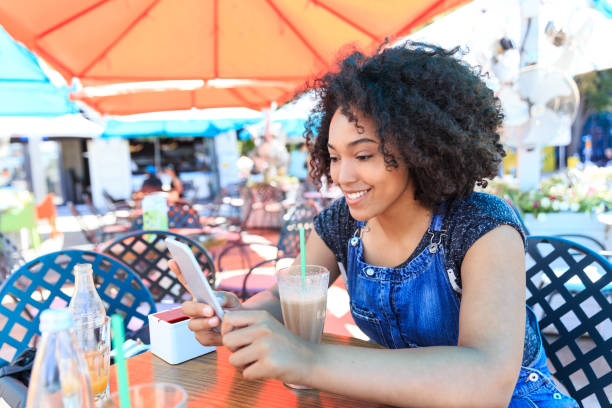 istock Smiling african woman drinking cocktail in cafeteria and using smart phone 1035073308