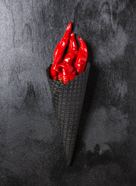 istock Red chili pepper symbolizing torch with fire on dark background. Hot pepper in a black Ice cream cone 1035080920