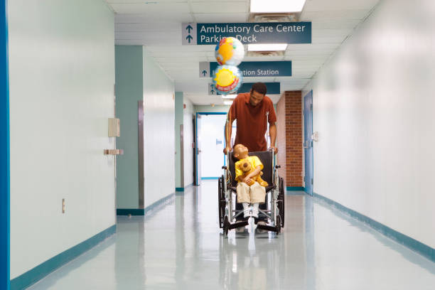 африканский отец толкает сына в инвалидной коляске по больничному коридору - balloon child elementary age people стоковые фото и изоб�ражения