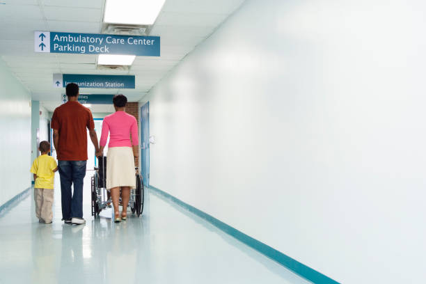 widok z tyłu afrykańskiej rodziny idącej korytarzem szpitalnym z wózkiem inwalidzkim - departure hall zdjęcia i obrazy z banku zdjęć