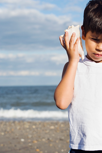 Young Hispanic boy listening to seashell