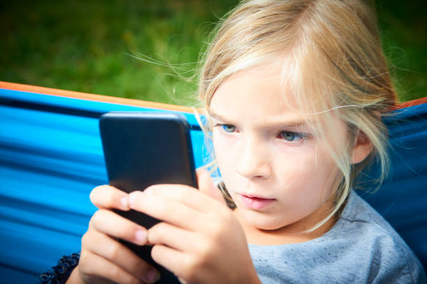 istock Child blond girl playing with a smart phone while lying on hammock outdoors 1035101044
