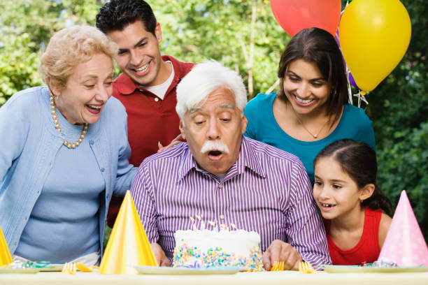 Senior Hispanic man blowing out birthday candles with family in park Senior Hispanic man blowing out birthday candles with family in park birthday wishes for daughter stock pictures, royalty-free photos & images