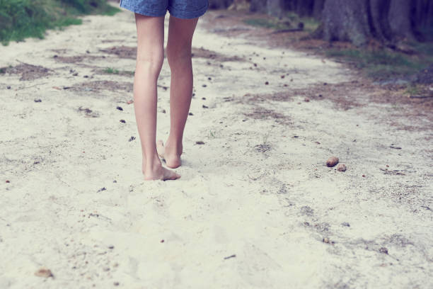 istock Child girl bare feet walking along the forest sandy path. 1035101360