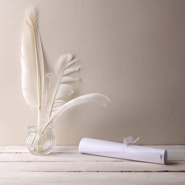 istock Paper roller and white quill feathers in glass bottle on white wood table. 1035117880