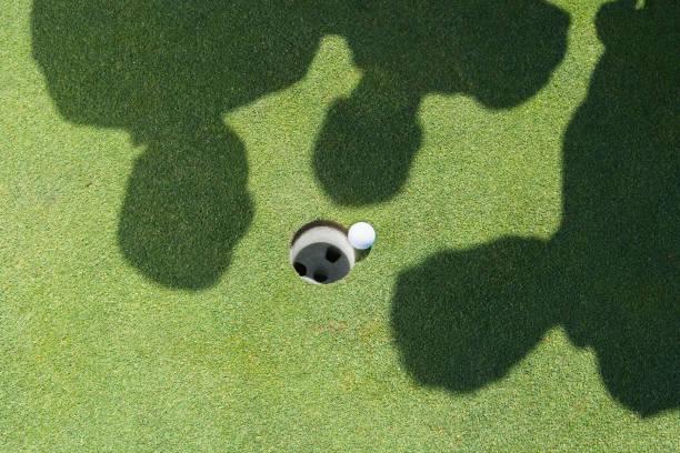 Shadows of golfers over golf ball next to hole Shadows of golfers over golf ball next to hole drive ball sports photos stock pictures, royalty-free photos & images