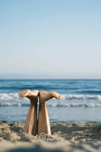 Mixed Race woman's feet sticking out of sand